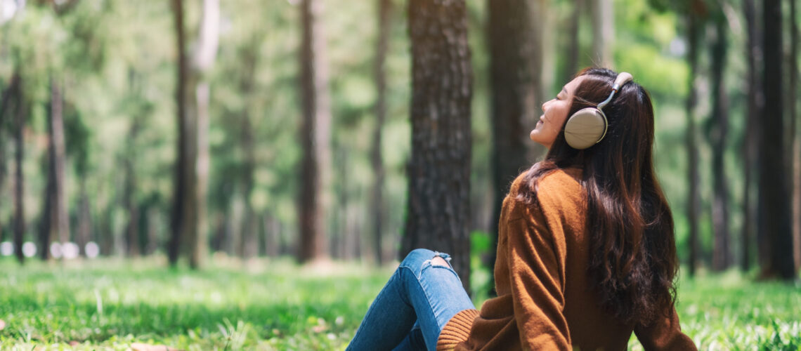 A beautiful asian woman enjoy listening to music with headphone with feeling happy and relaxed in the park